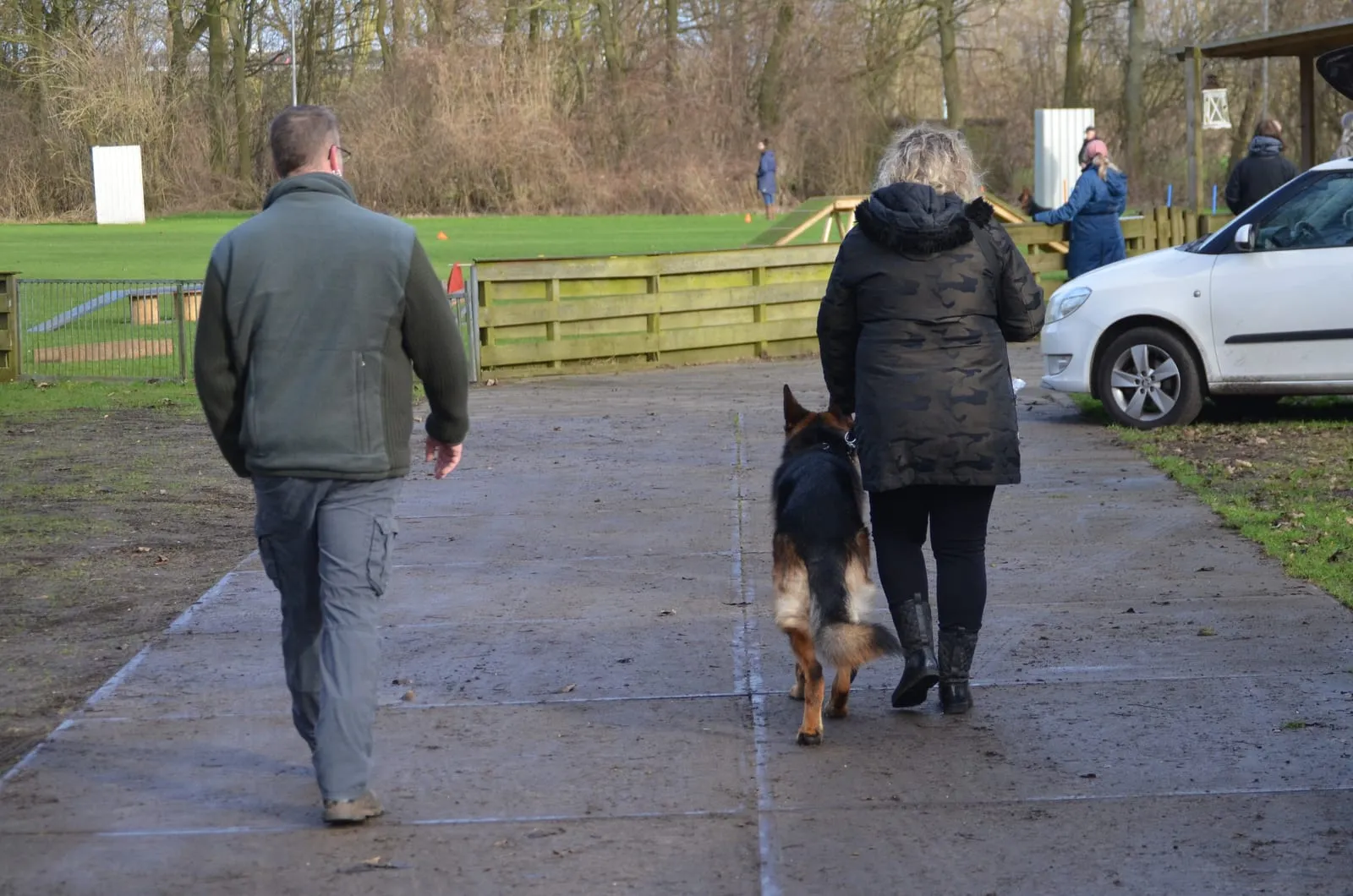 Twee cursisten lopen met een Duitse herder over het pad naar het trainingsveld